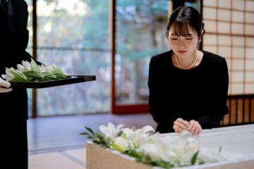 棺に百合の花を置く喪服の女性