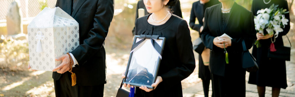 遺影を持つ喪服の女性と遺骨を持つも風の男性